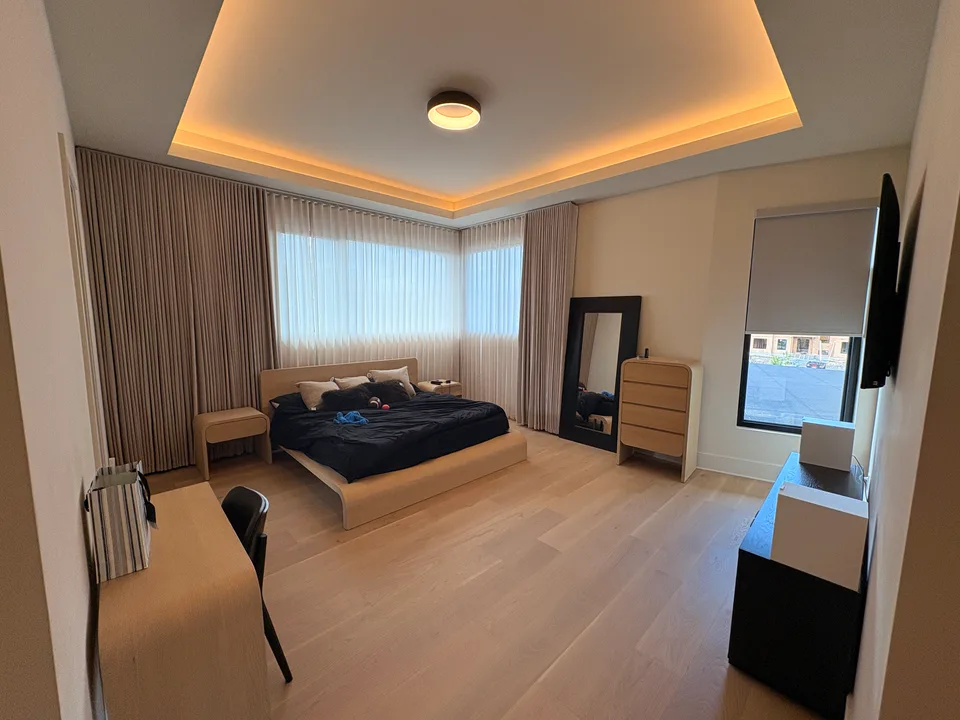 Custom corner-window drapery and a roller shade in a spacious bedroom