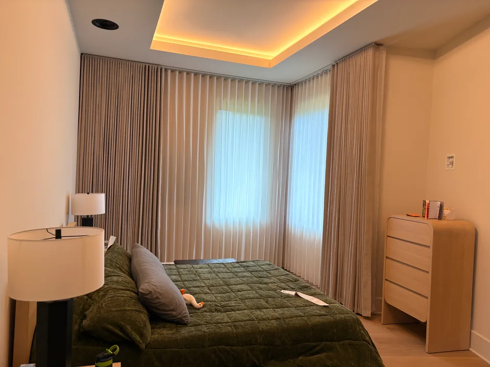 Layered corner-window curtains beside a green quilted bed
