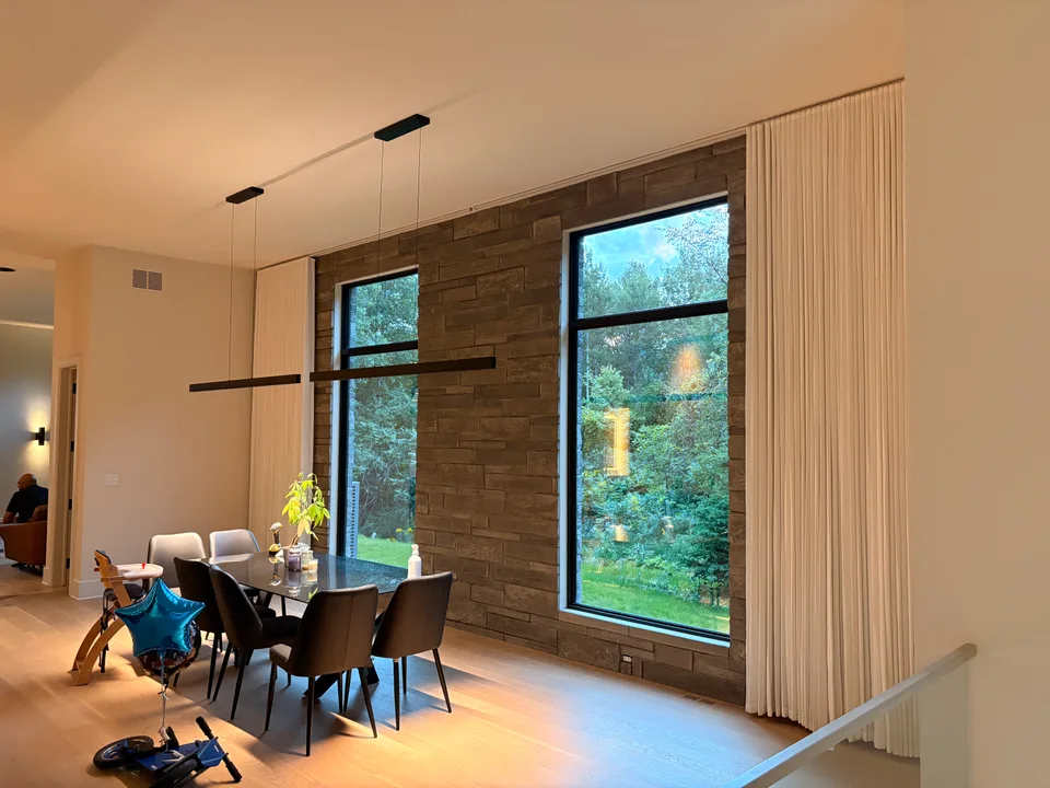 Tall white curtains framing dining room windows beside a stone feature wall